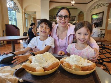 a mom with her two children smiling at the camera with two plates of very large doughnuts in front of them