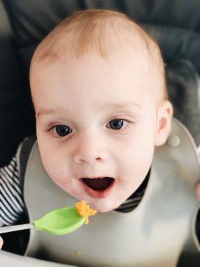 7 month old boy open mouth to eat sweet potato from green baby spoon