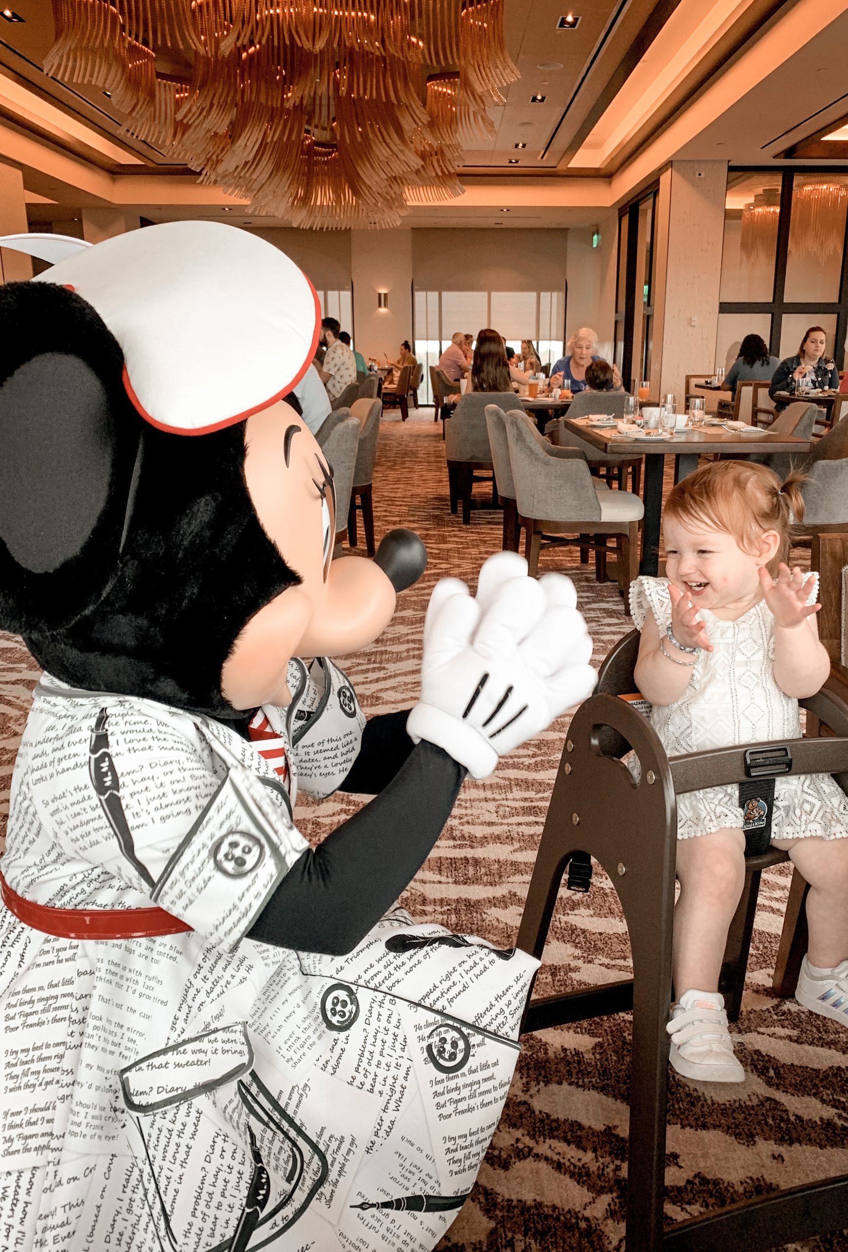 little girl in highchair clapping with Minnie Mouse beside her