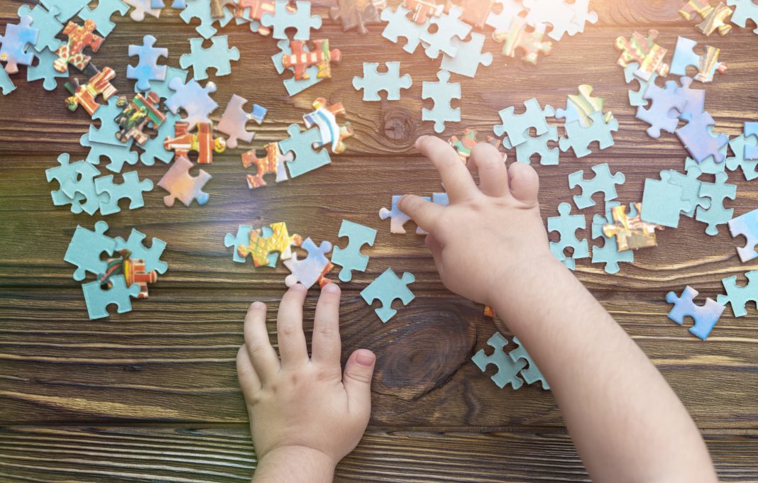 A child's hand collects a puzzle on a wooden background.