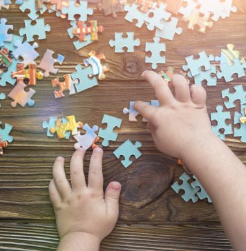 A child's hand collects a puzzle on a wooden background.