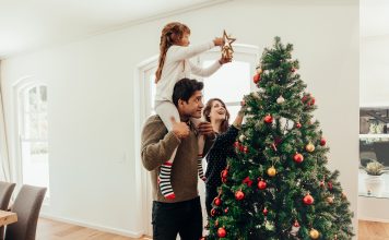 Family decorating a Christmas tree. Young man with his daughter on his shoulders helping her decorate the Christmas tree.