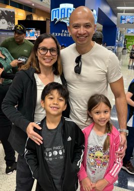 Family of four - mom in glasses, dad with sunglasses in collar of his shirt, boy with gray and black jacket and girl in pink jacket at the Kia Center