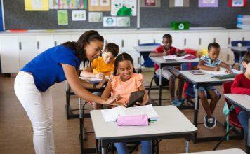 African american female teacher teaching disabled girl to use digital tablet at elementary school. school and education concept