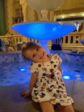 little girl in front of a blue lit up fountain