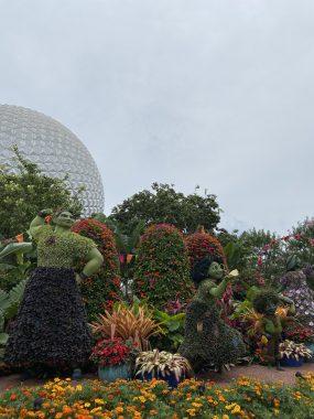 Encanto's Lousia, Mirabel and Antonio made of flowers in front of trees and Spaceship Earth