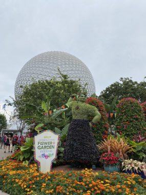 Encanto's Lousia made of flowers in front of trees and Spaceship Earth