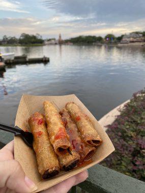 five eggrolls in brown plate with fork and lagoon behind