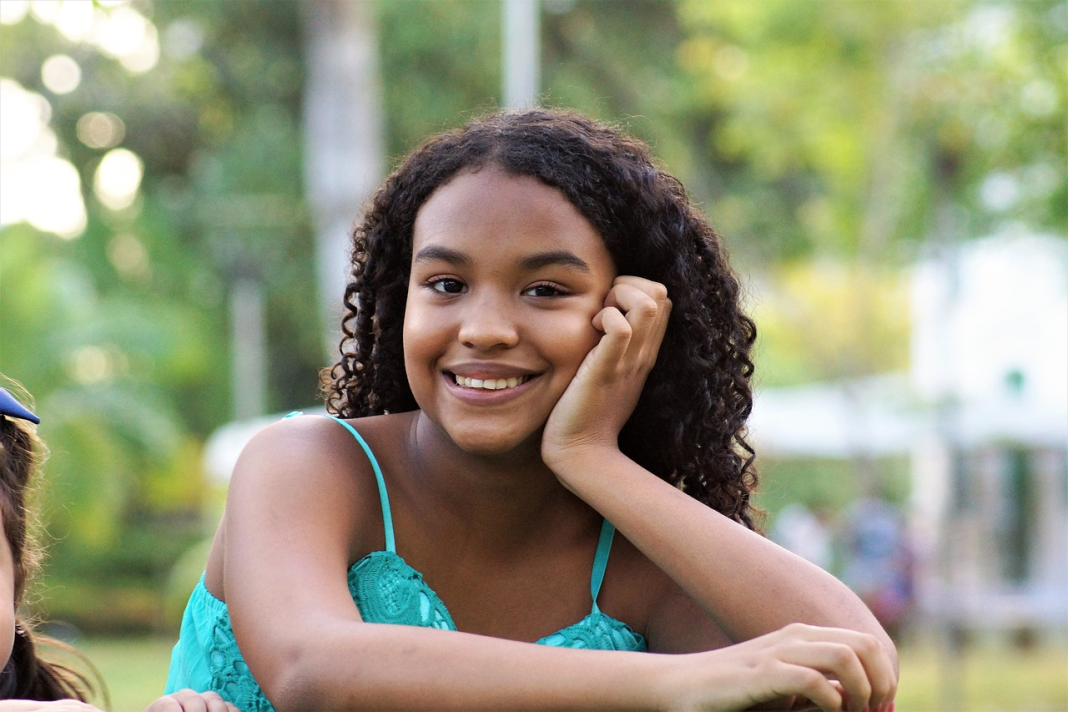 Dark brown girl teen with dark hair smiling and staring into the camera.