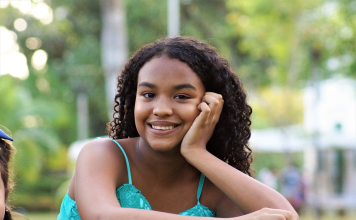 Dark brown girl teen with dark hair smiling and staring into the camera.