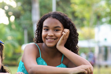 Dark brown girl or teen with dark hair smiling and staring into the camera. 