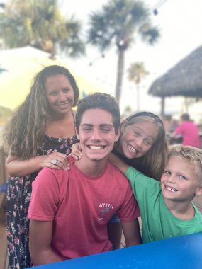 a mom and three children (two boys, one girl) smiling at the camera with red cheeks and tanned skin. benefits of traveling with the family