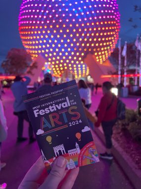 Festival of the Arts Passport in front of a red, orange and purple lit Spaceship Earth