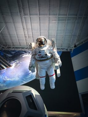 astronaut floating in space with Earth behind and space station