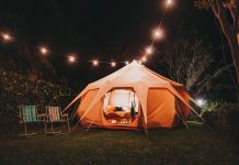 a tent outside lit up from within and string lights overtop for backyard camping