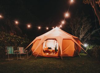 a tent outside lit up from within and string lights overtop for backyard camping
