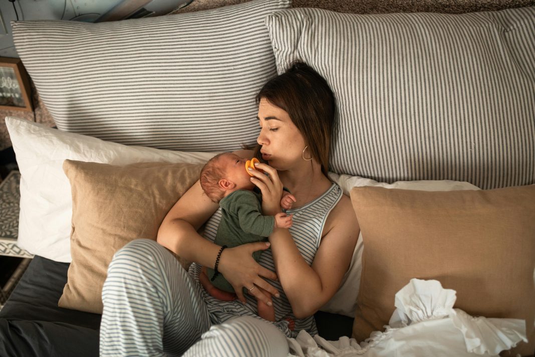 mom cuddling newborn baby in bed. Beauty and Wellness Tips for Postpartum Recovery