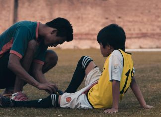 young athletes sitting on ground, while older athlete or coach teaches him about sports safety and ties his shoes
